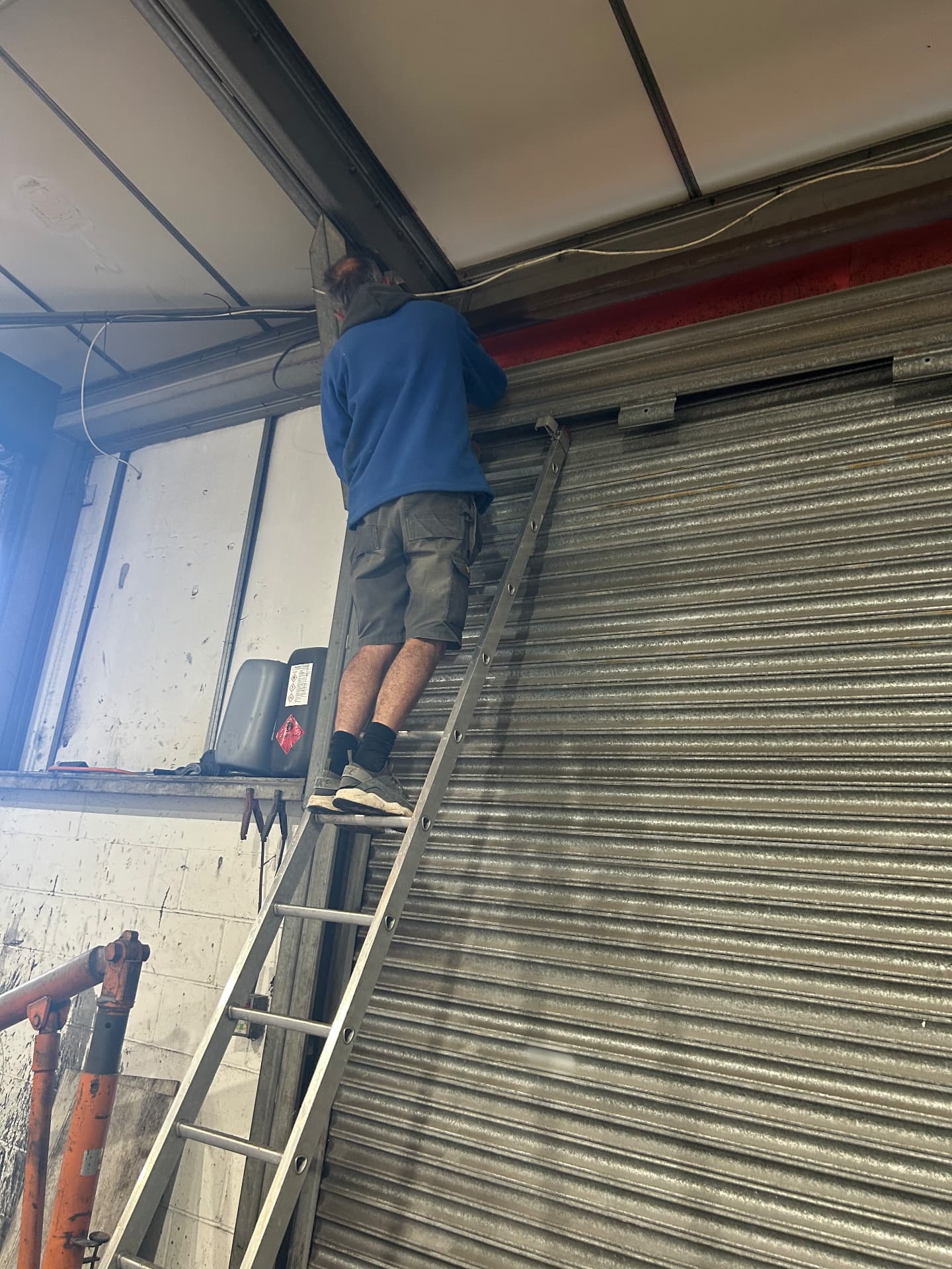 Excel engineer on a ladder repairing a roller shutter mechanism